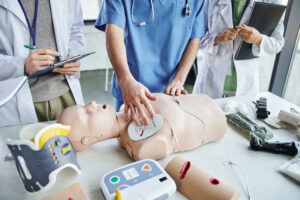 Healthcare professionals practicing Advanced Cardiovascular Life Support (ACLS) training with a CPR manikin and defibrillator.
