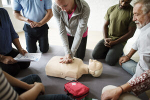 A group of adults participating in instructor-led ACLS training while practicing chest compressions on a CPR mannequin.