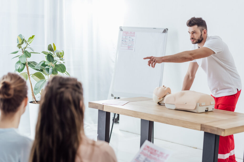 Instructor-led CPR course held in a room with instructor pointing towards he audience 