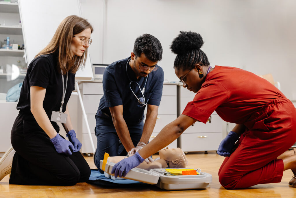 Diverse group of medical students practicing chest compressions and AED use on an infant mannequin during pediatric life support training session.