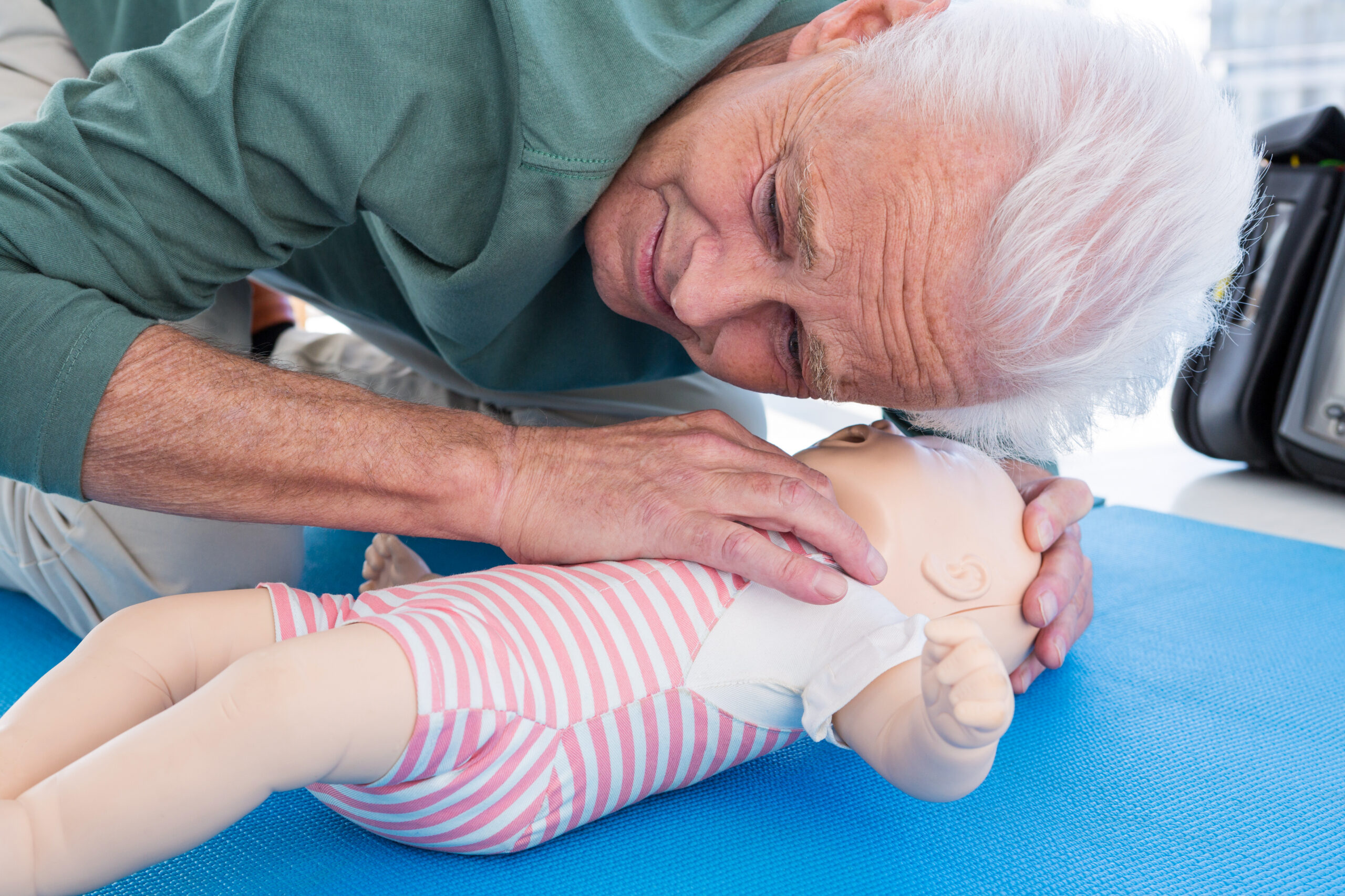 Older adult performing infant CPR by checking airway on a pediatric training mannequin during hands-on PALS training.